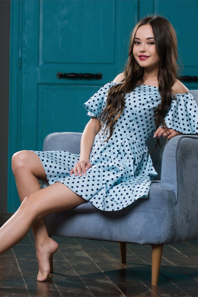 Красивая девушка в платье в горох на кресле