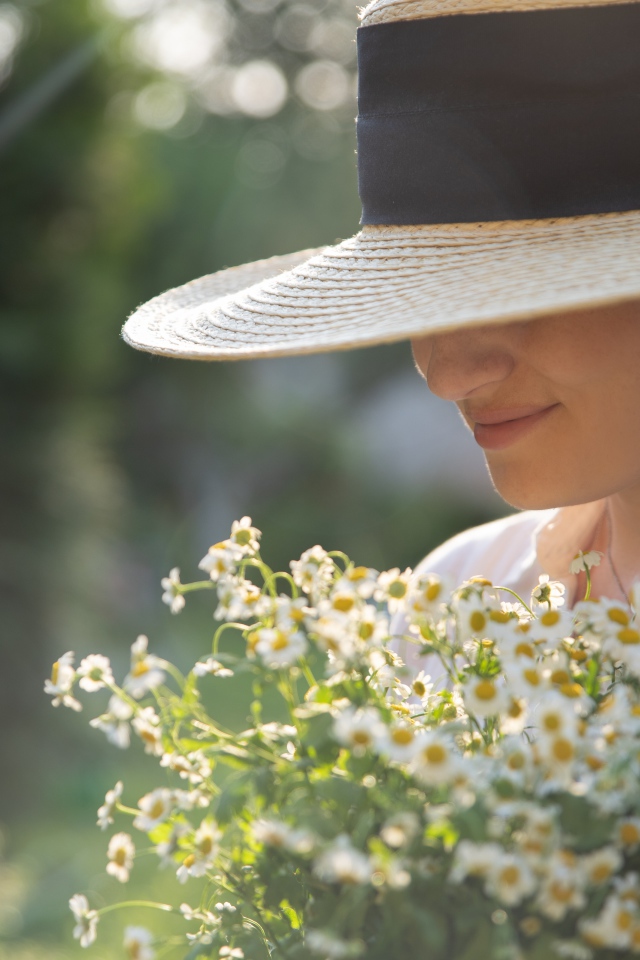 Красивая девушка в шляпе с букетом ромашек 