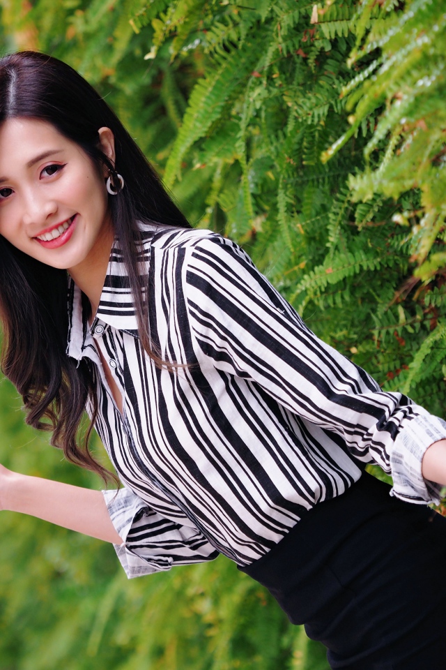 Красивая девушка в полосатой рубашке стоит у растения