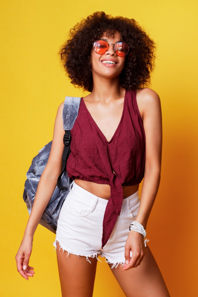 Красивая девушка в очках с рюкзаком на желтом фоне 