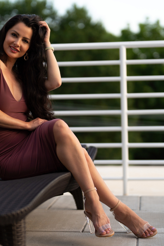 Красивая стильная брюнетка в платье сидит на диване