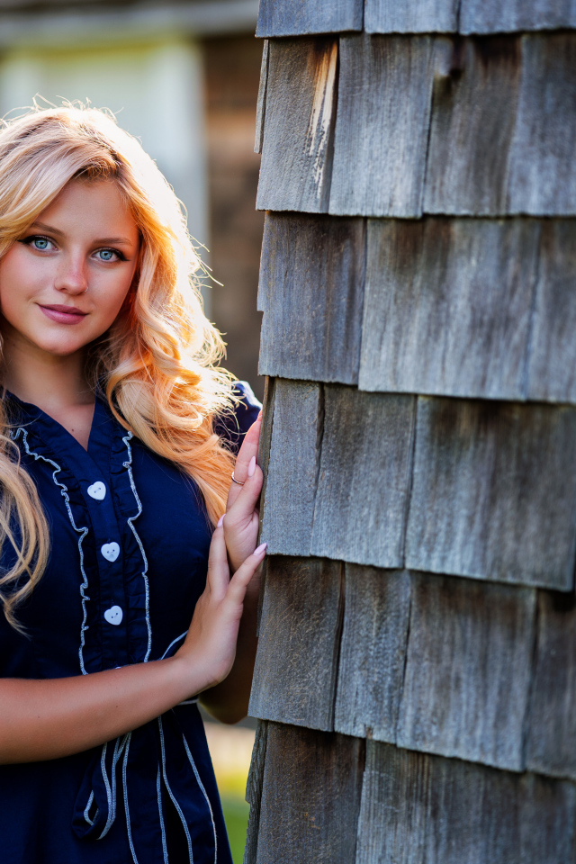 Голубоглазая блондинка в платье стоит у стены 