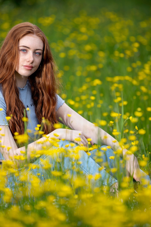 Голубоглазая девушка сидит на поле с желтыми цветами
