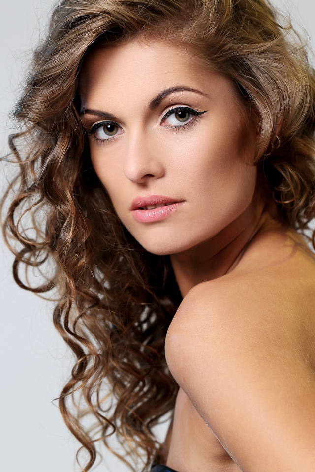 Вьющиеся волосы у красивой девушки на сером фоне