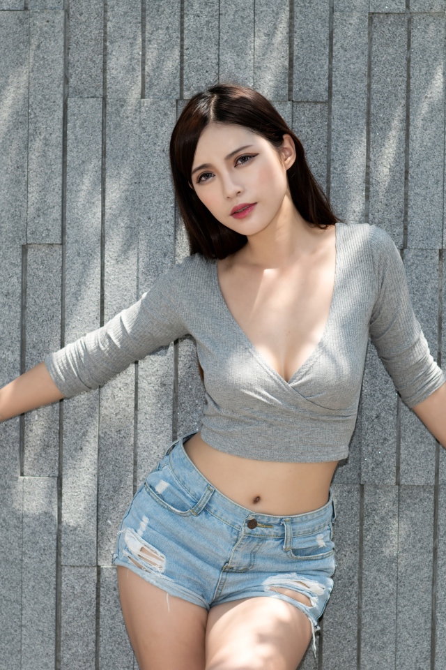 Милая девушка в серой кофте у стены 