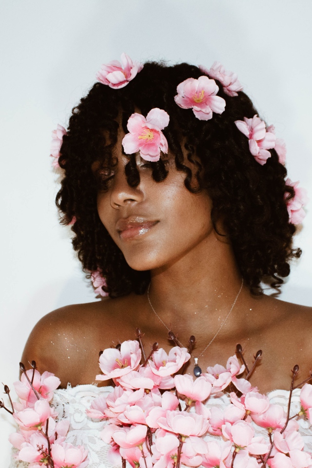 Темнокожая девушка в розовых цветах на сером фоне