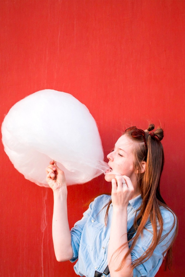 Девушка ест сладкую вату на красном фоне 