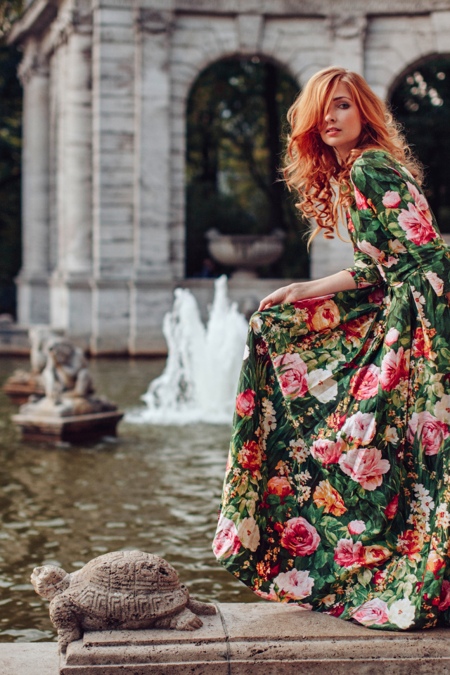 Девушка в красивом цветастом платье у пруда в парке 