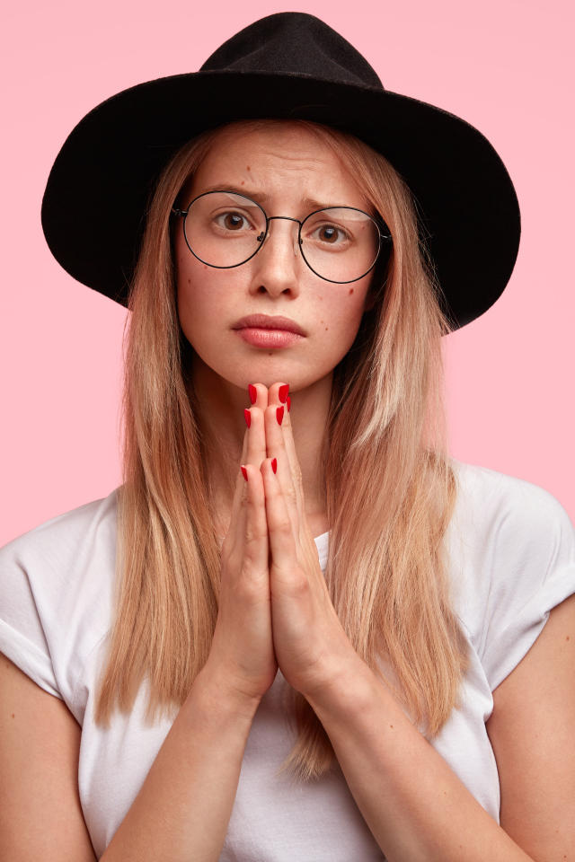 Girl in a black hat on a pink background asks for forgiveness