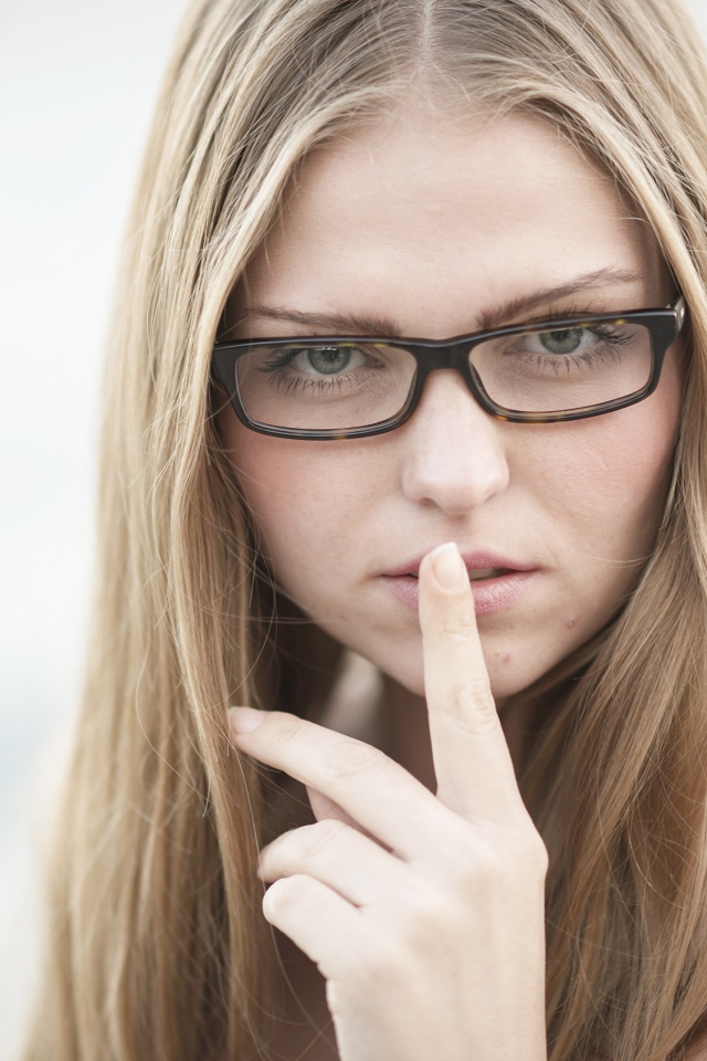 Девушка в очках с пальцем у лица
