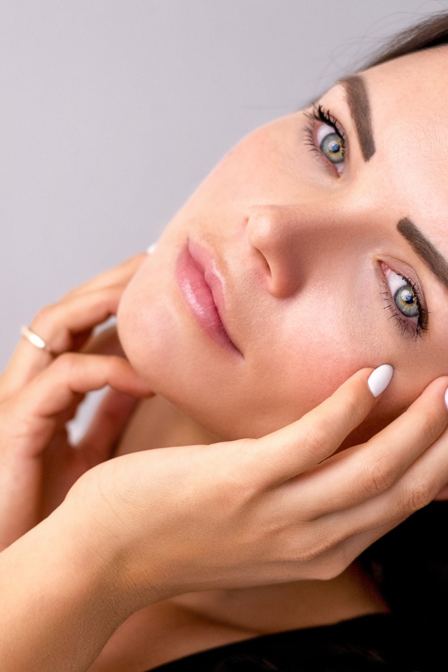 Девушка с руками у лица на сером фоне