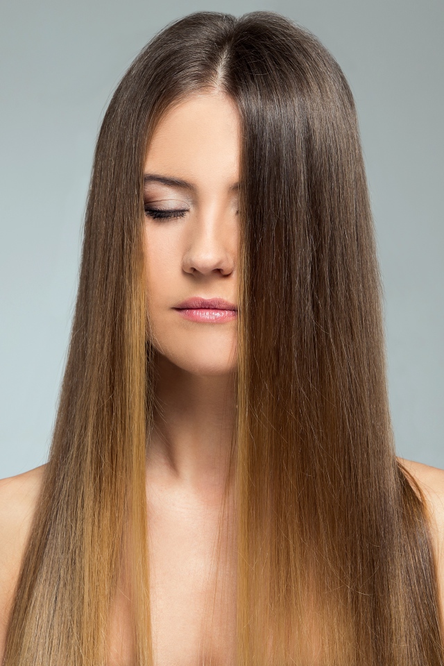 Длинноволосая шатенка с закрытыми глазами на сером фоне 