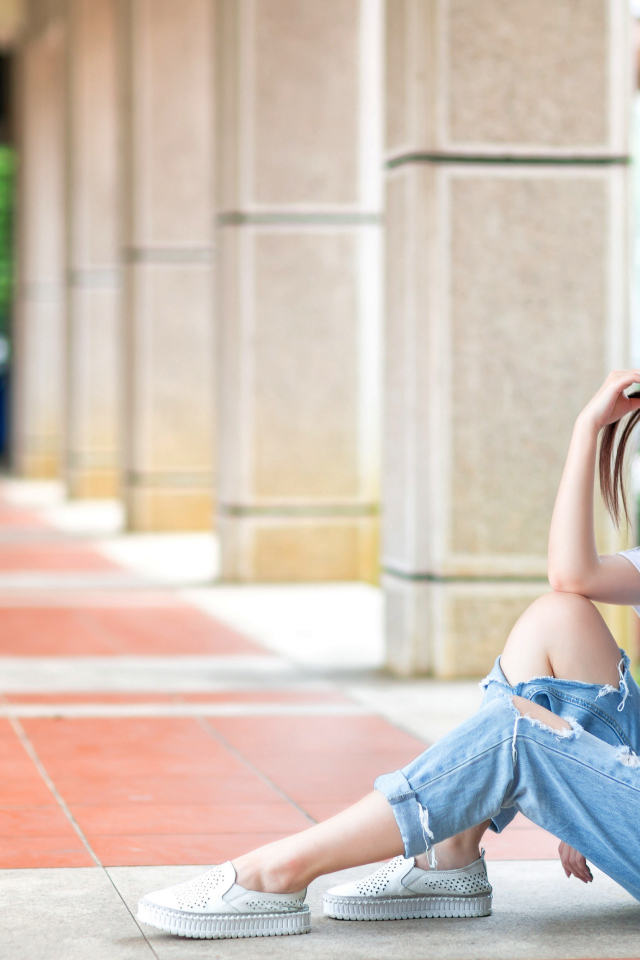 Грустная девушка азиатка сидит у колонны