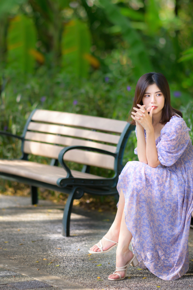 Грустная девушка азиатка в платье на лавке в парке 