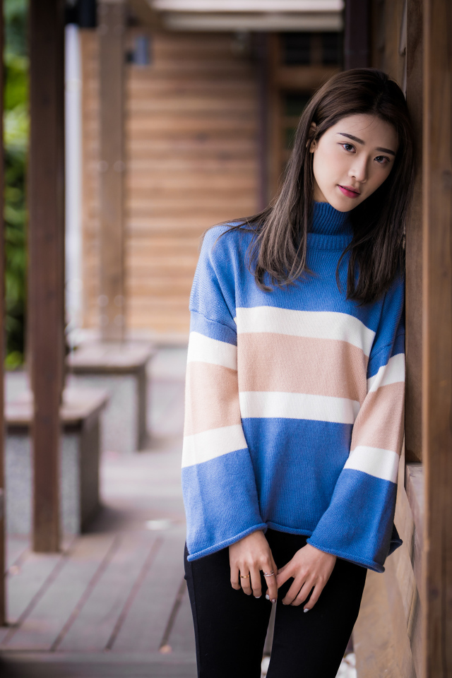 Грустная девушка азиатка в свитере у стены 