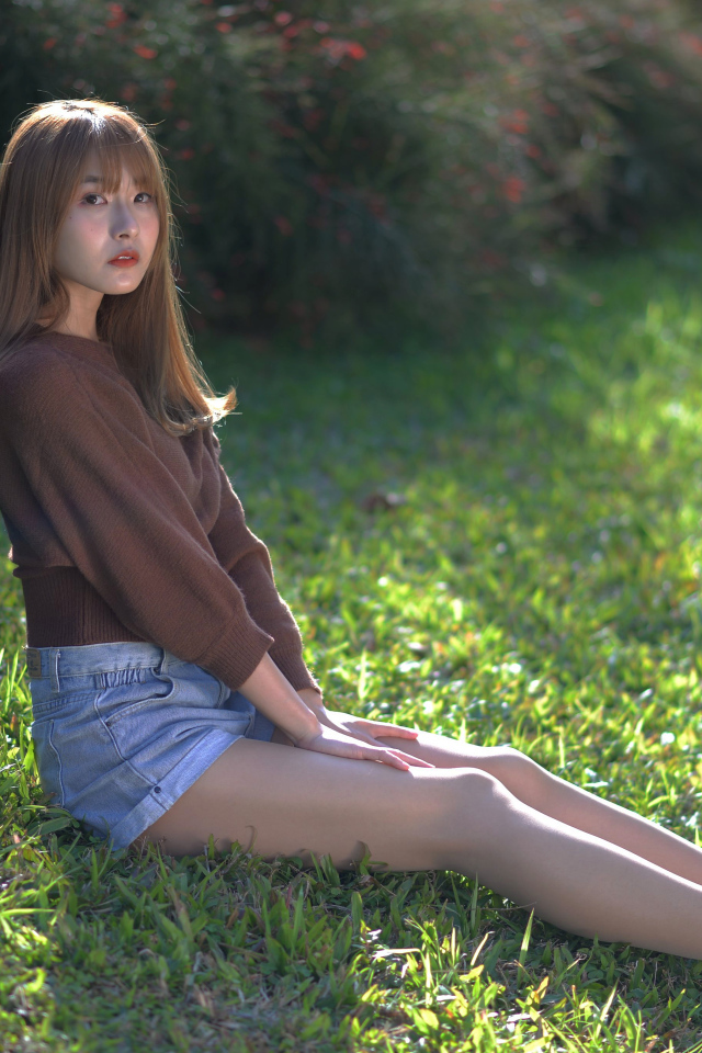 Грустная девушка азиатка сидит на зеленой траве 