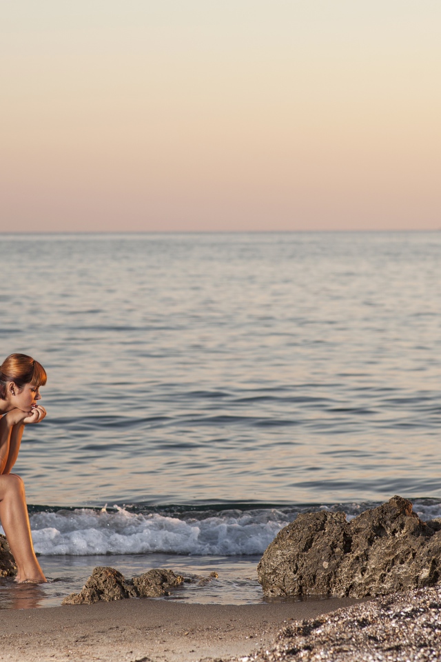 Грустная девушка сидит на камне у моря