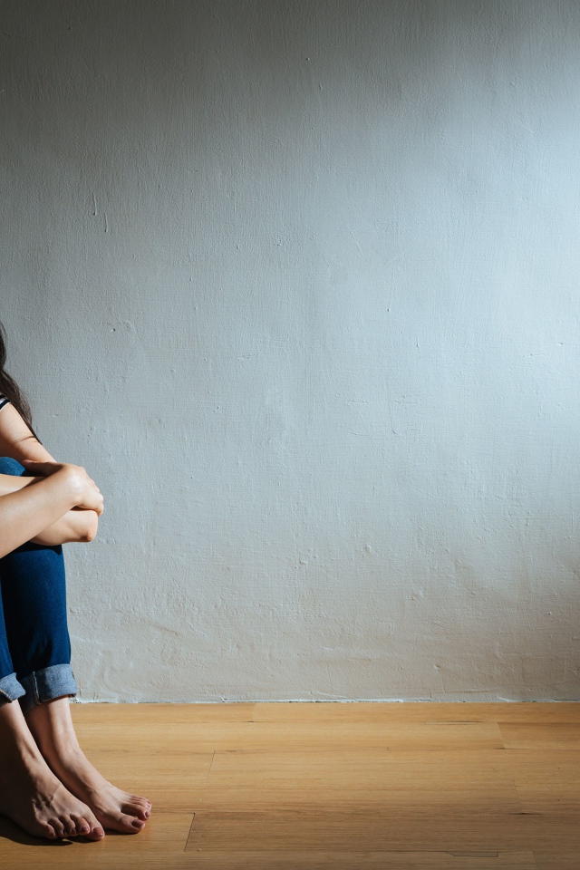 Испуганная девушка азиатка сидит у стены