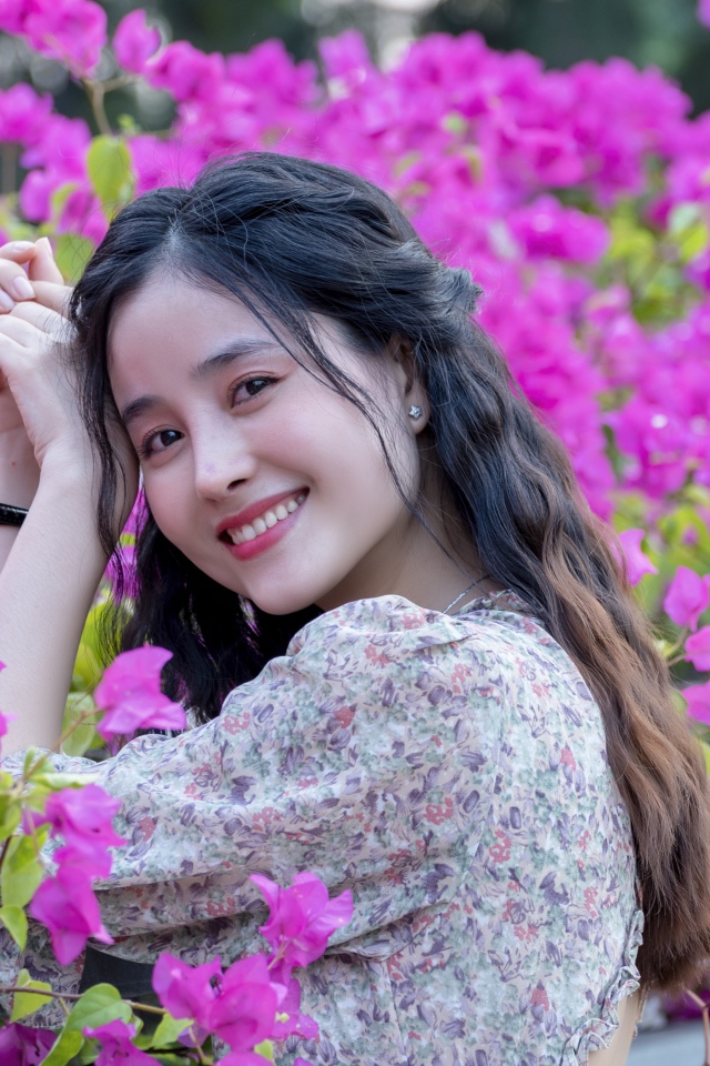 Улыбающаяся девушка азиатка на фоне розовых цветов