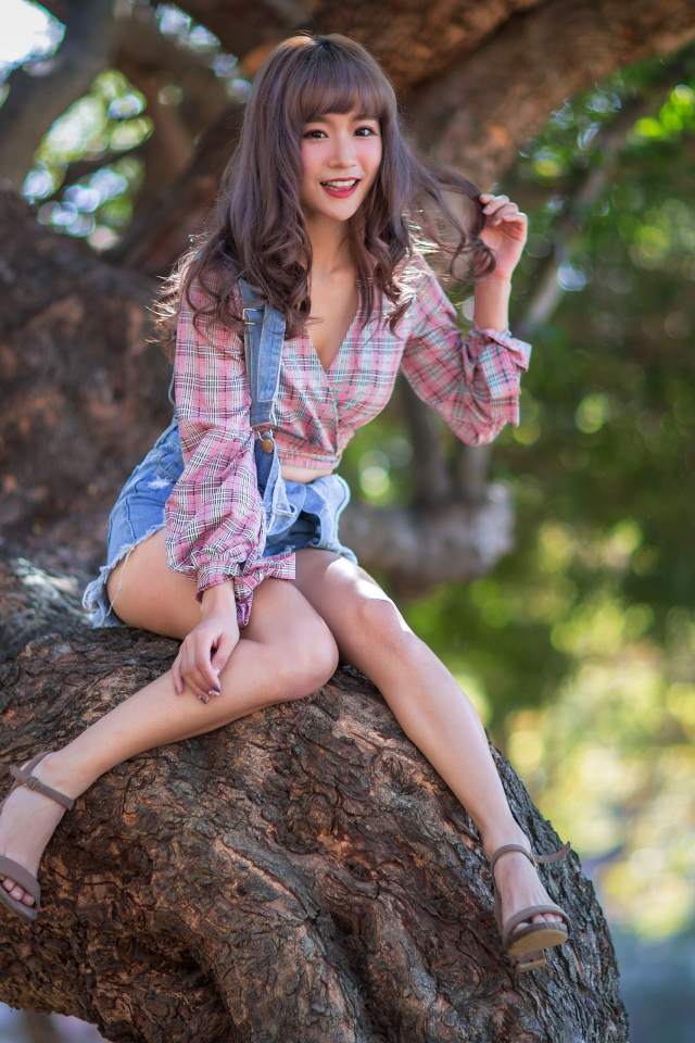 Улыбающаяся девушка азиатка сидит на дереве