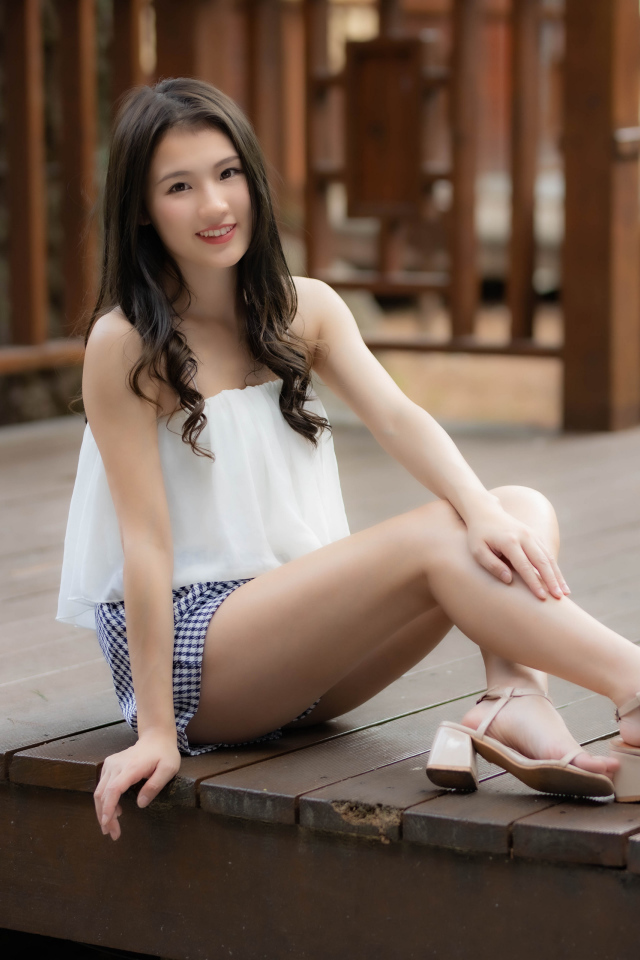 Улыбающаяся девушка азиатка сидит на мосту 