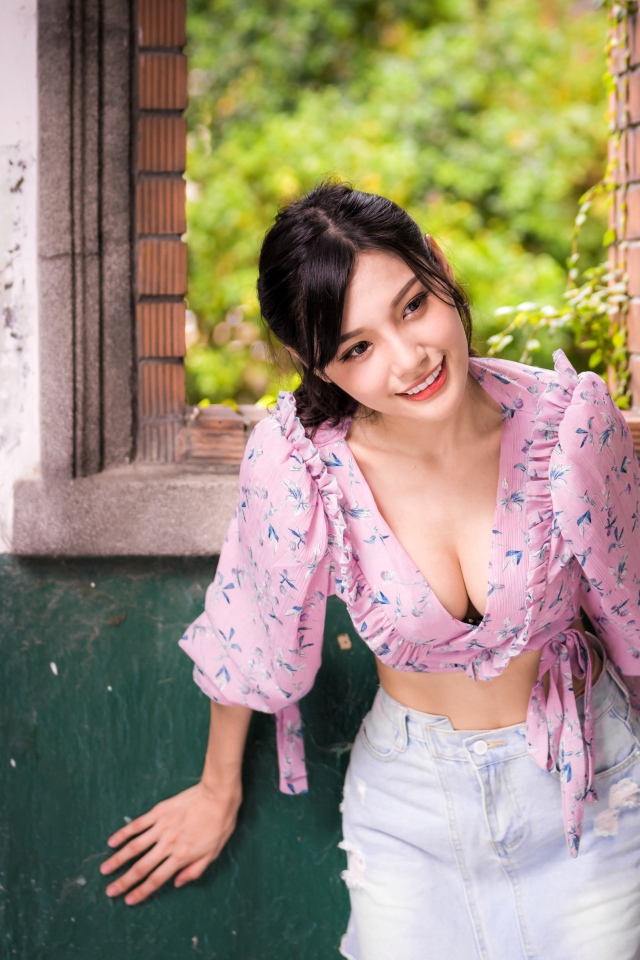 Улыбающаяся девушка азиатка стоит у окна 