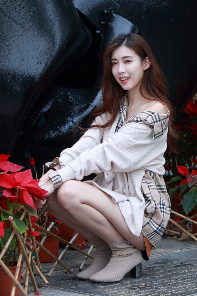 Улыбающаяся азиатка сидит у красных цветов 