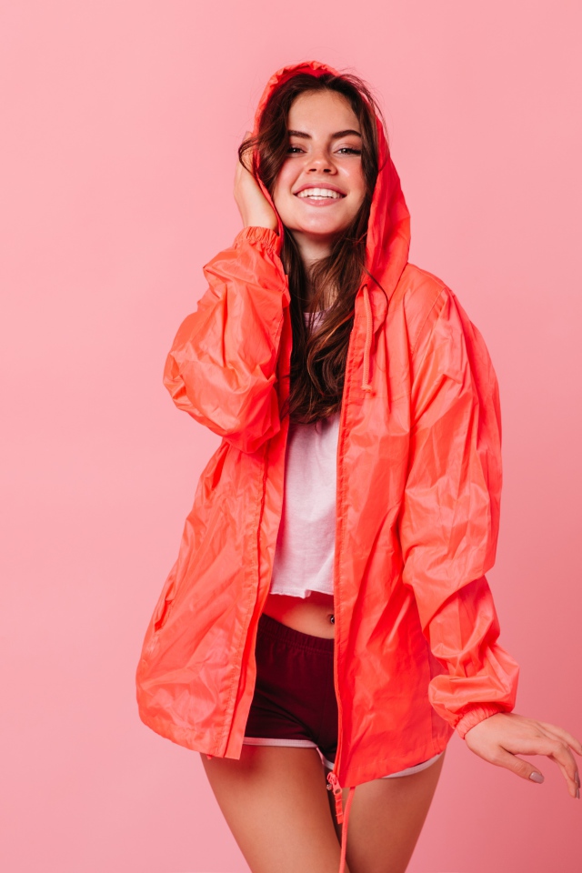 Улыбающаяся девушка в плаще на розовом фоне