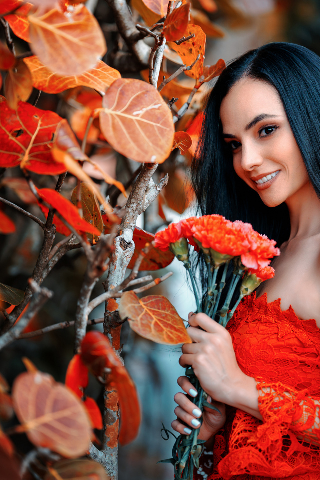 Улыбающаяся девушка с букетом гвоздик у стены с осенними листьями