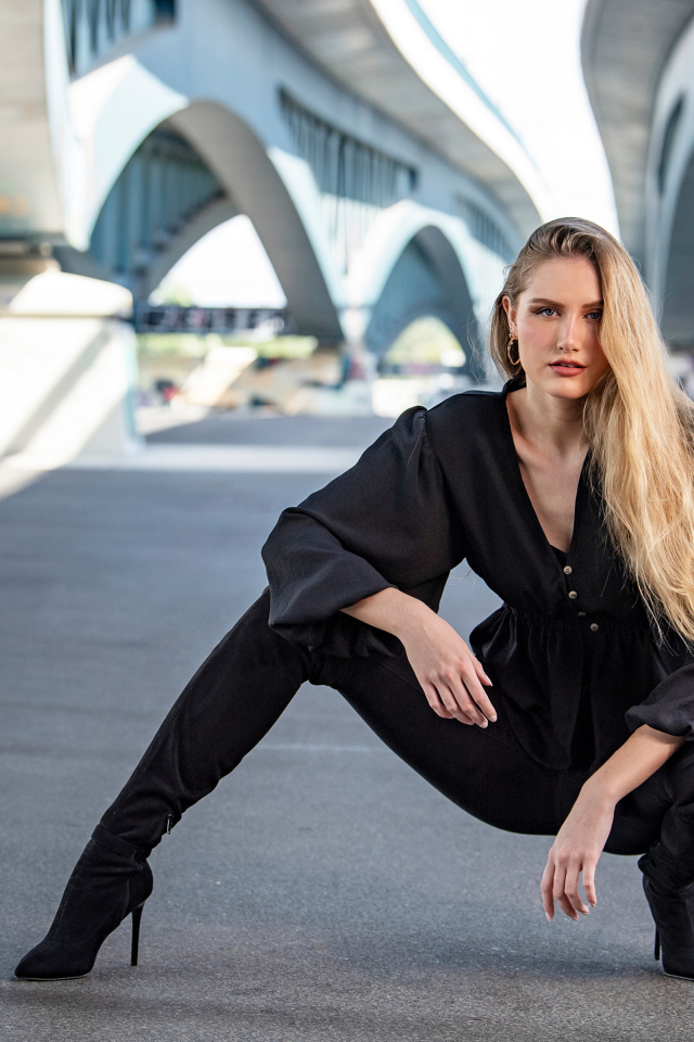 Стильная девушка в черном костюме под мостом