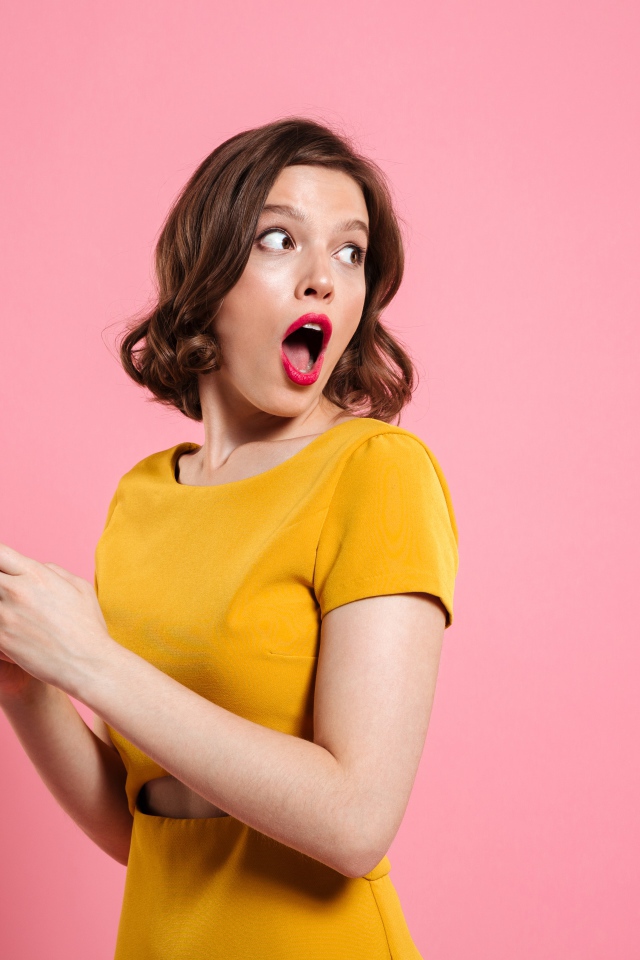 Удивленная девушка с телефоном в руках на розовом фоне