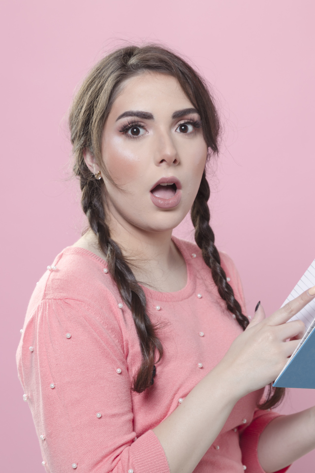 Удивленная девушка с книгой на розовом фоне