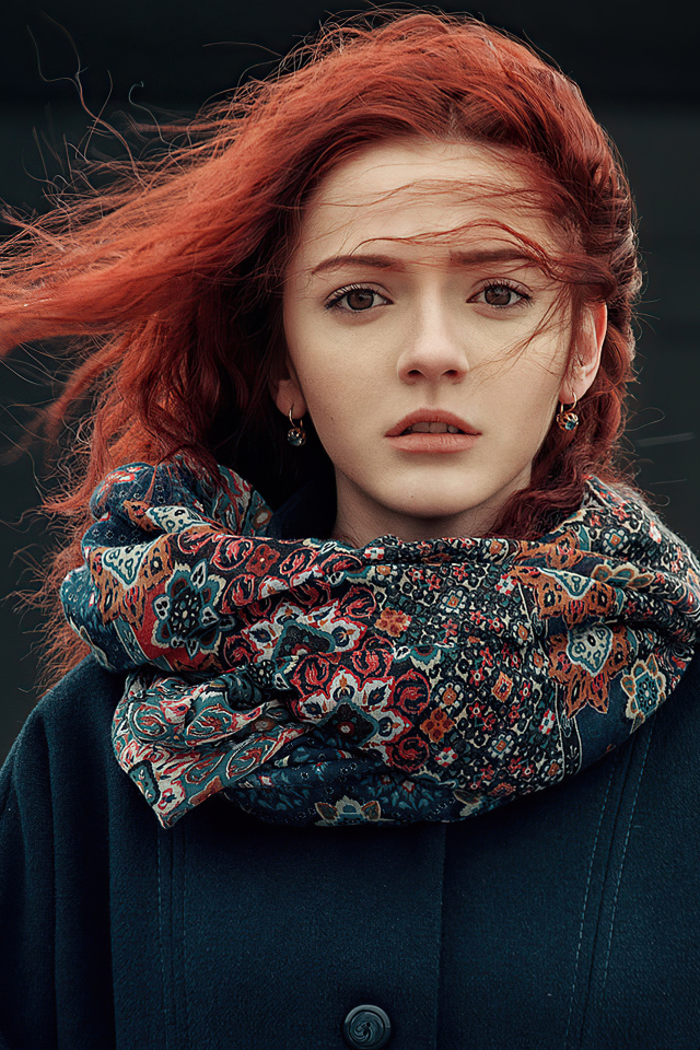 Ветер развивает волосы рыжеволосой девушки в пальто