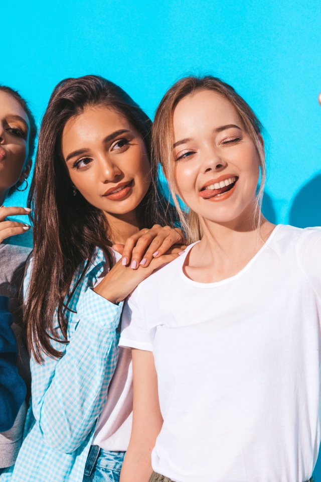 Три подруги делают селфи на голубом фоне