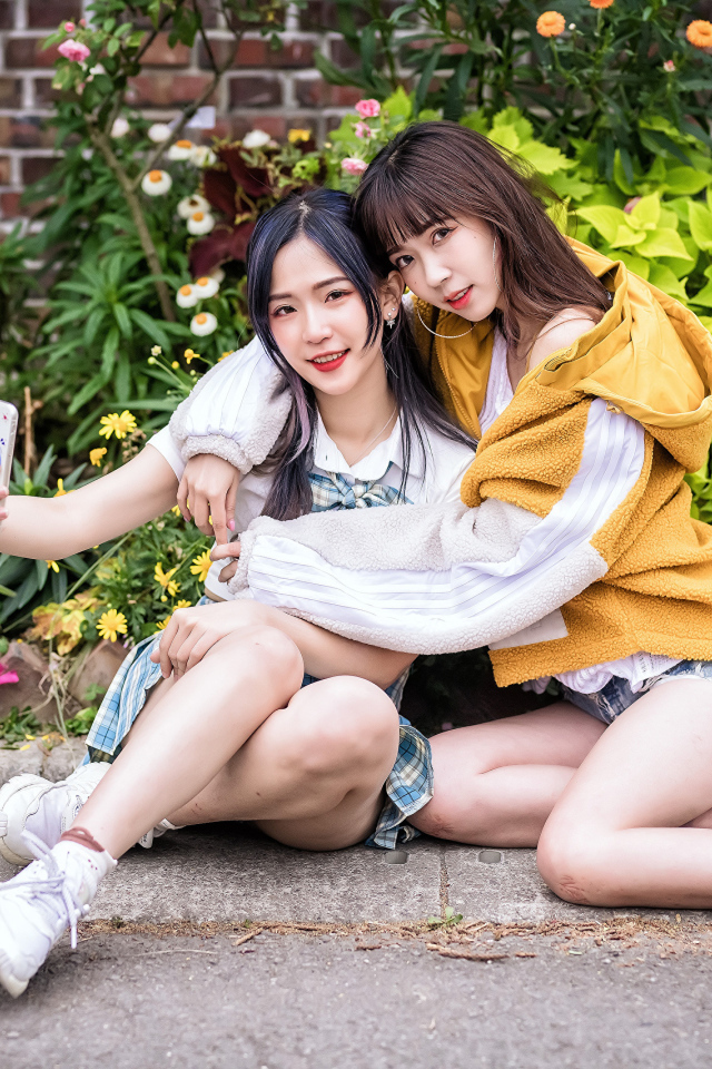 Две девушки азиатки сидят у стены с цветами 