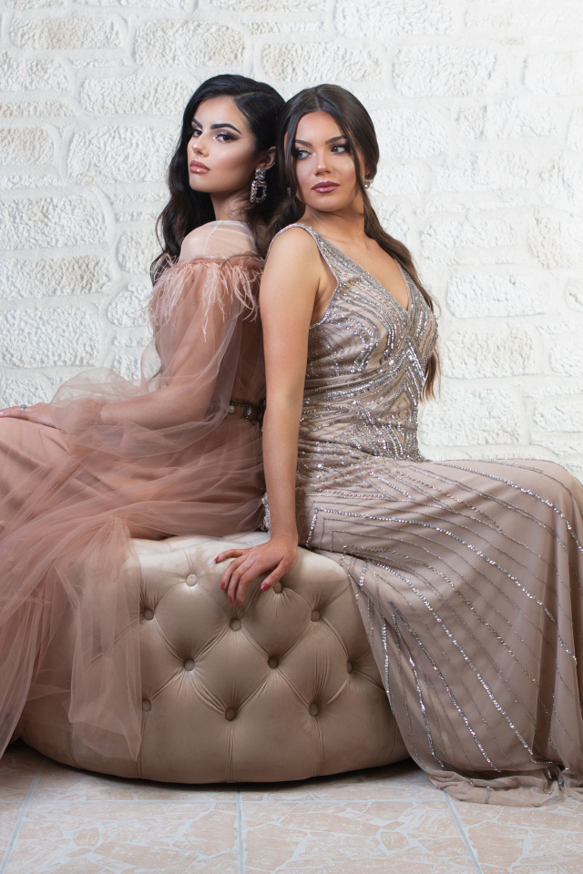 Две девушки в красивых платьях сидят на диване 