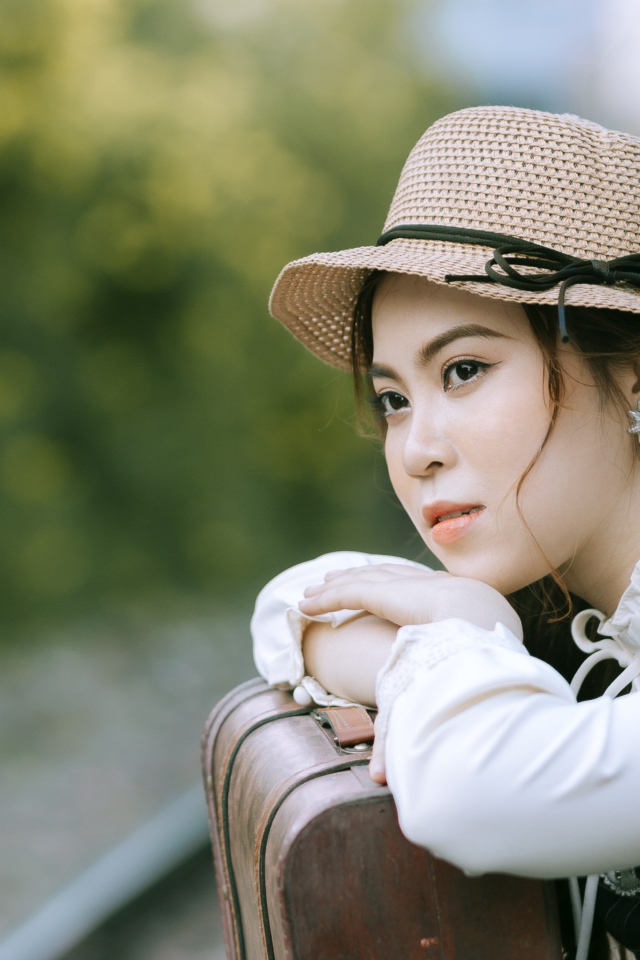 Молодая азиатка в шляпе с чемоданом