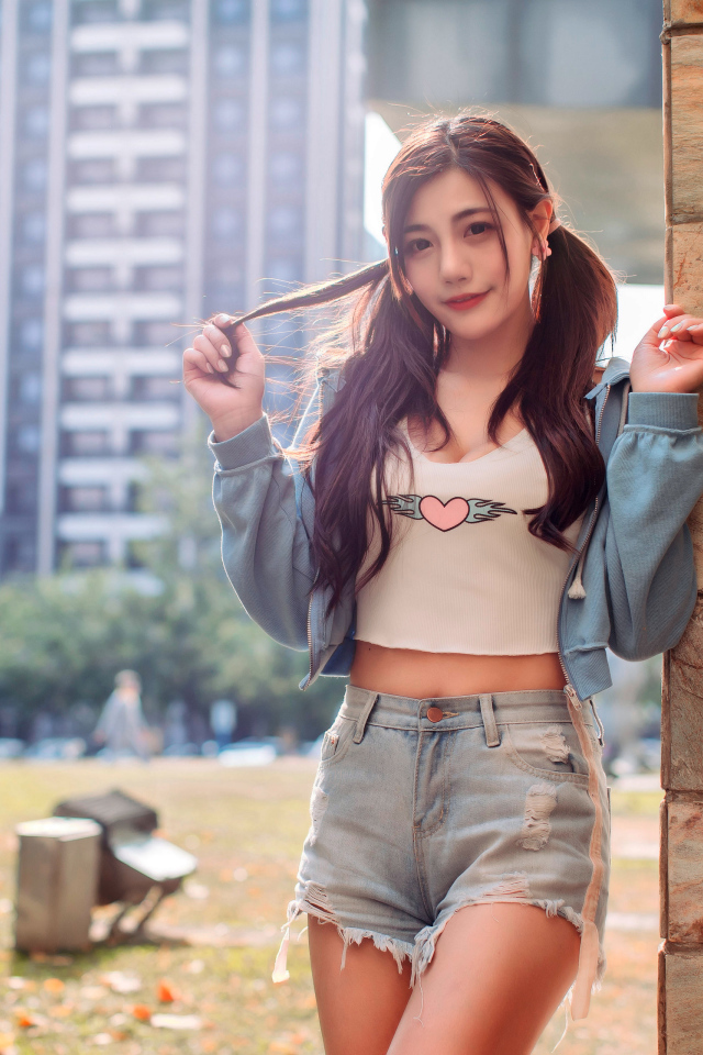 Молодая азиатка в коротких шортах стоит у стены