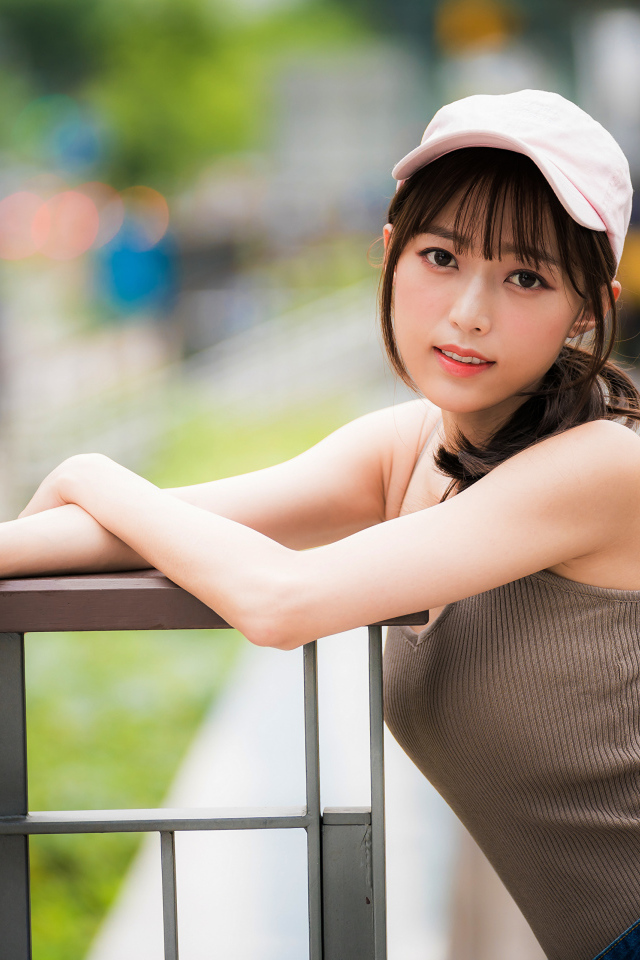 Молодая азиатка в кепке у перил 