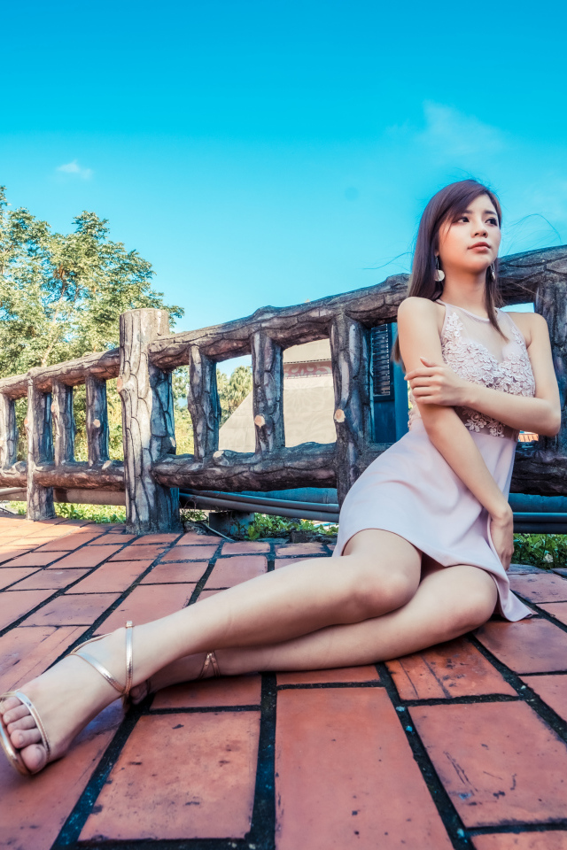 Молодая красивая азиатка сидит  на полу у забора