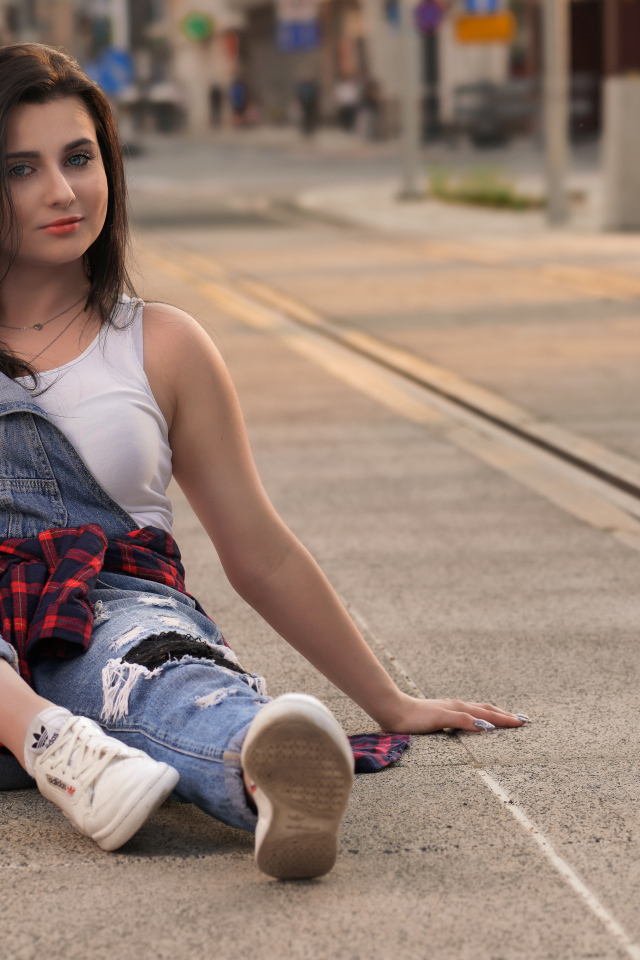 Молодая девушка в джинсовом наряде сидит на асфальте