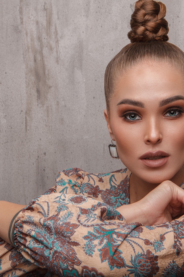 Молодая девушка с прической на голове на фоне стены