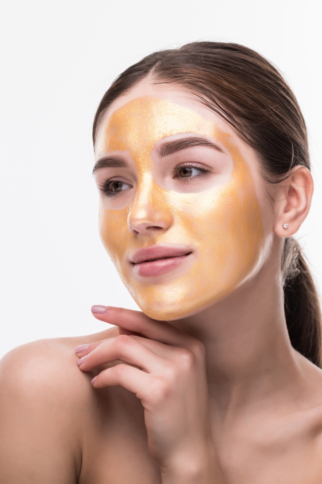 Молодая девушка без макияжа с золотой маской на лице