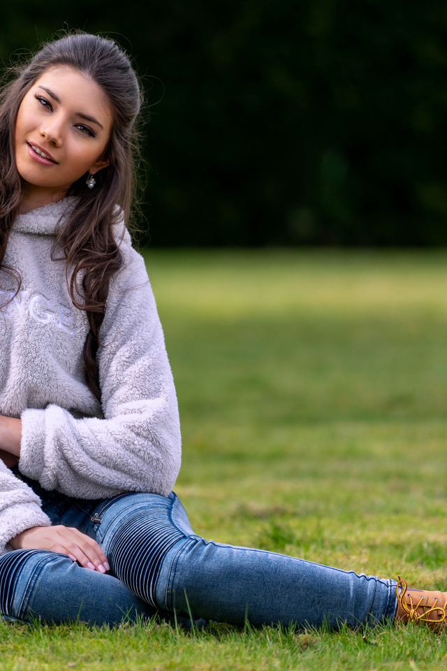 Молодая длинноволосая девушка сидит на траве 