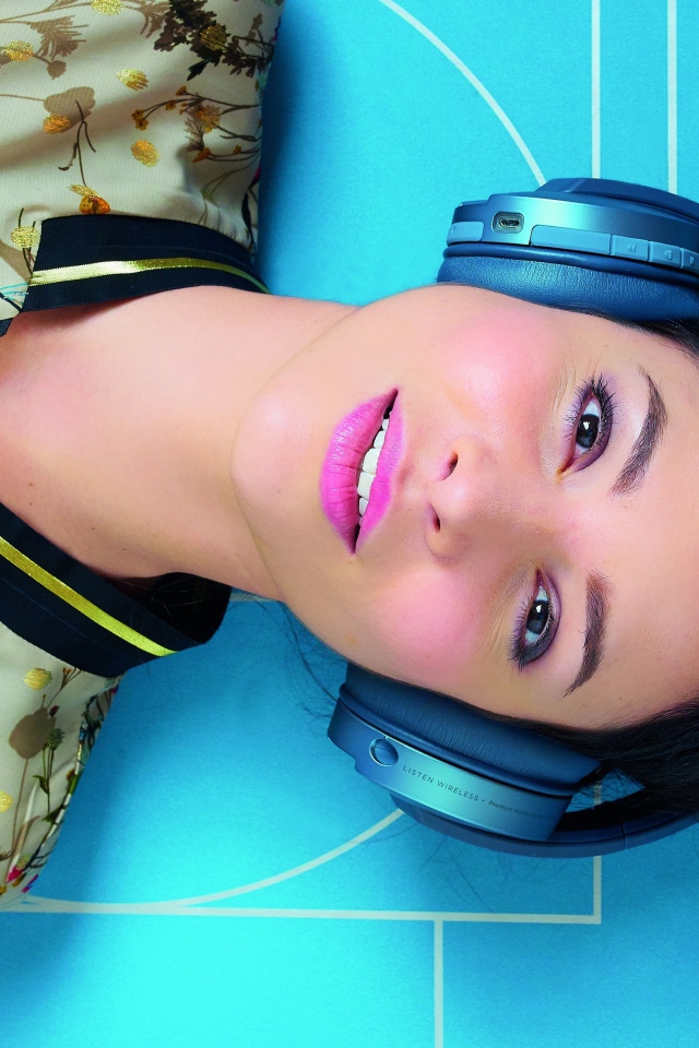 Молодая женщина в наушниках лежит на голубом полу