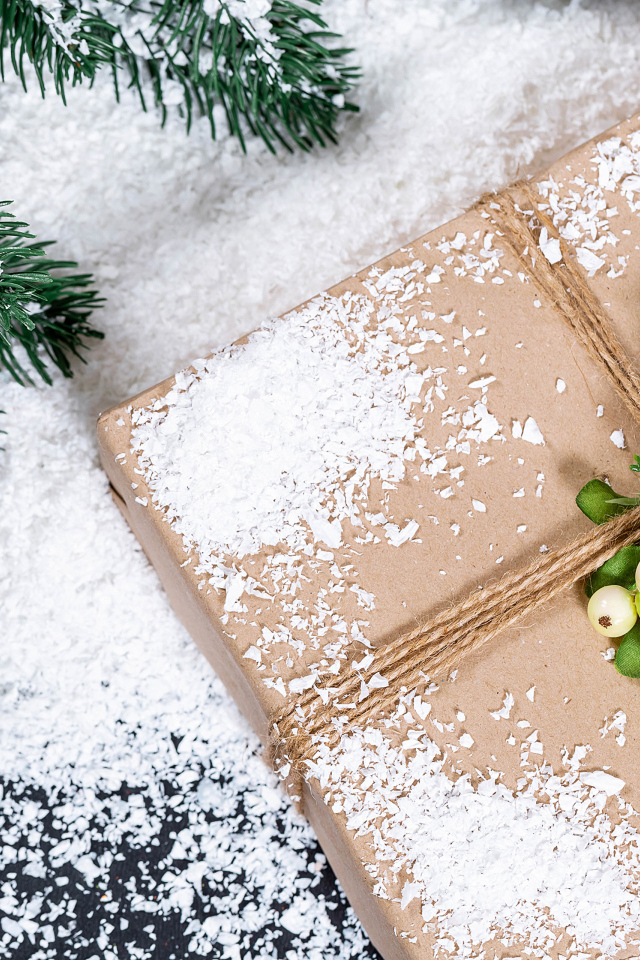 Подарок с заснеженной веткой ели на столе