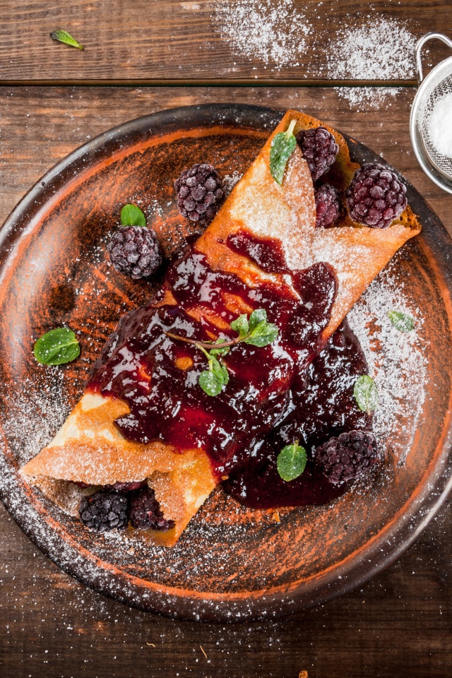 Блин с ягодами и джемом на тарелке с сахарной пудрой