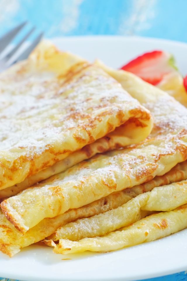 Румяные тонкие блинчики на тарелке с клубникой 