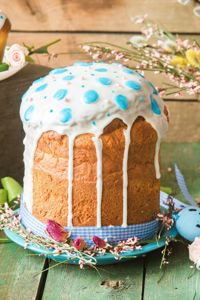 Красивый пасхальный кулич с белой глазурью на столе с цветами