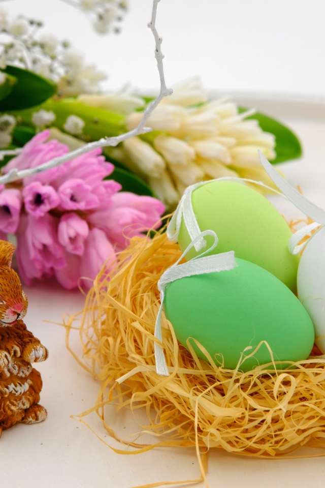 Три пасхальных яйца в гнезде на столе с цветами